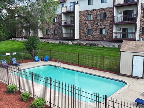 A pool surrounded by a black fence and a building in the background.