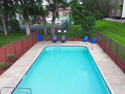 A small pool surrounded by a red fence and blue chairs.