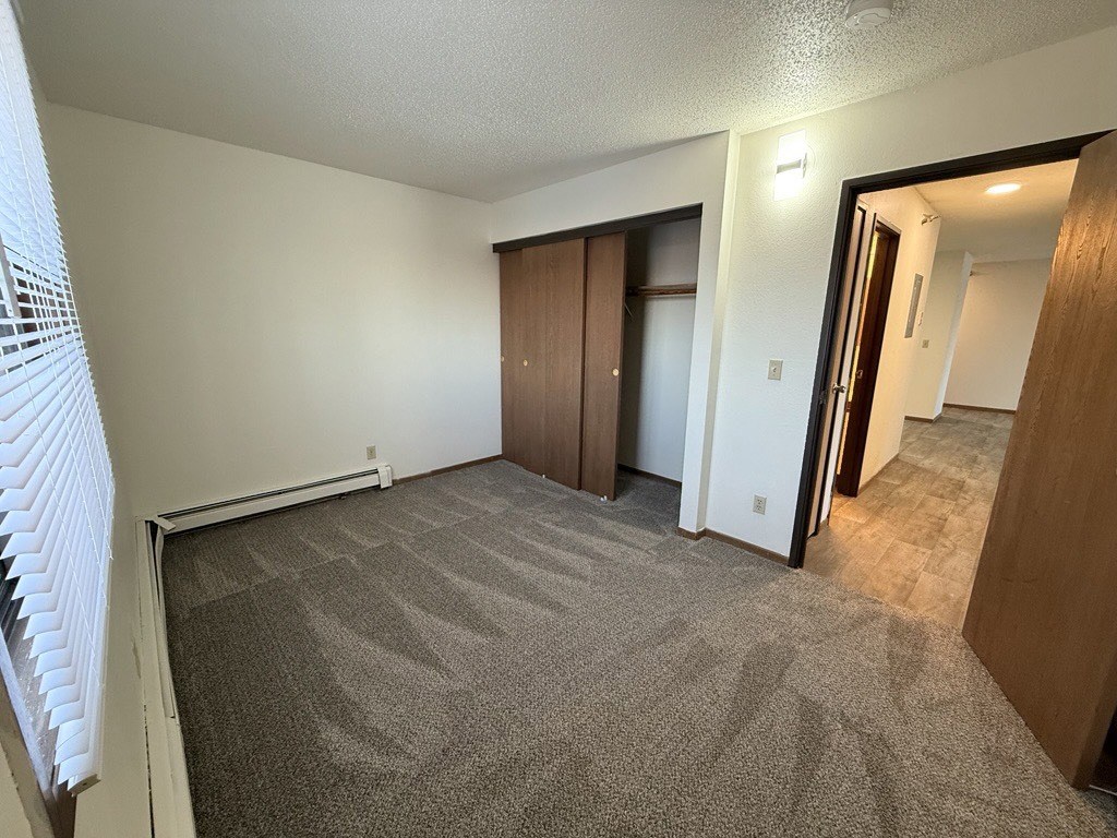 A room with carpeted floor and a window with blinds.