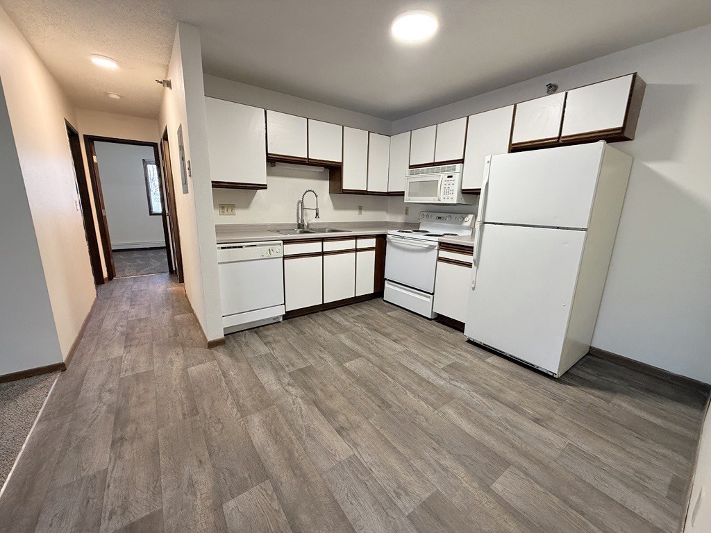 A kitchen with white appliances and wooden flooring.
