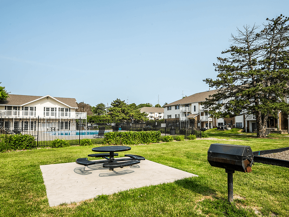 a picnic table and grill sit on a concrete slab in a grassy area with a pool