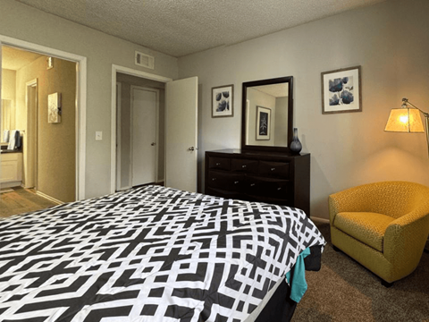 A bedroom with a black and white patterned bedspread, a yellow chair, and a dresser with a mirror.