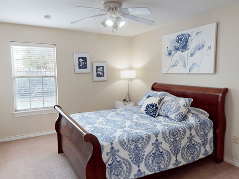 A bedroom with a bed, a ceiling fan, and two framed pictures on the wall.