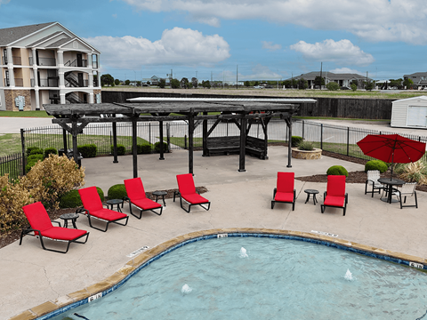 A pool with red chairs and a black umbrella.