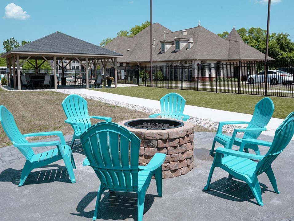 a fire pit with four blue adirondack chairs in front of a gazeb
