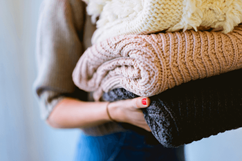 A person holding a stack of knitted sweaters.
