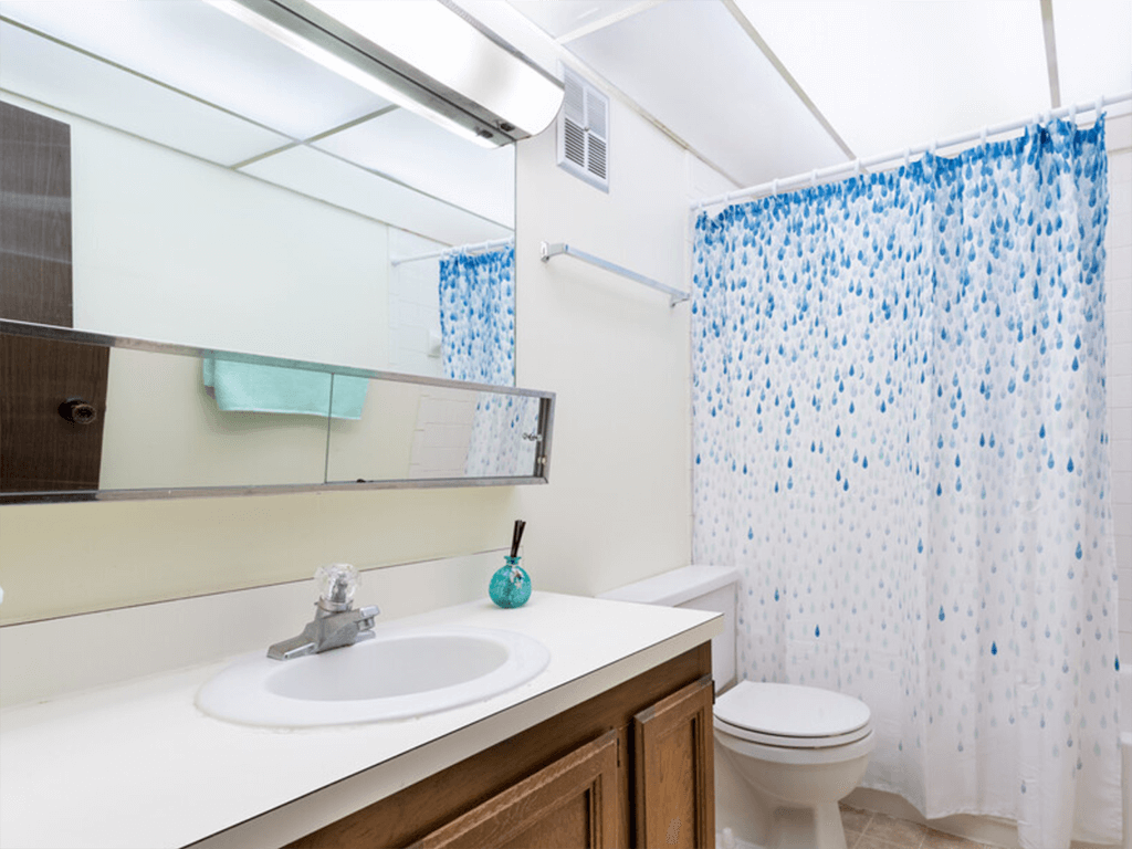 A white sink with a blue soap and a blue toothbrush in a bathroom with a white toilet and a shower curtain with blue dots.