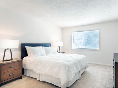 A bedroom with a bed, nightstands, and a window.