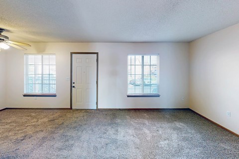 A room with a carpeted floor, two windows, and a door.