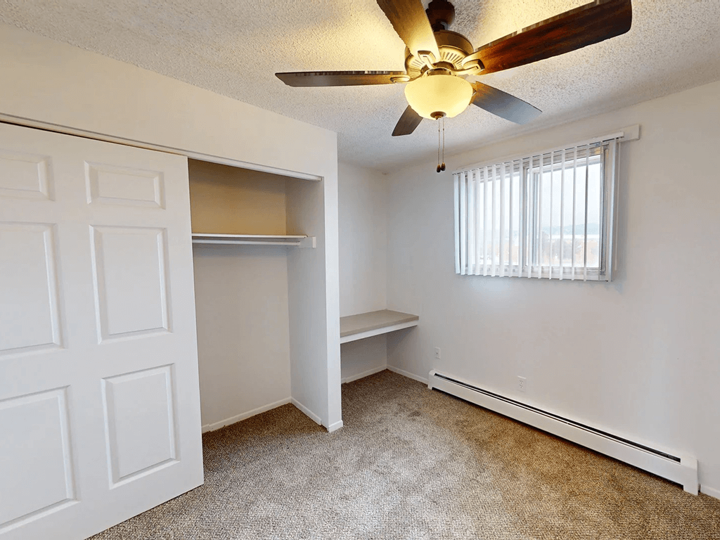 A room with a ceiling fan and a window with blinds.