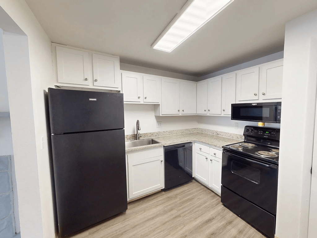 A black refrigerator is in a kitchen with white cabinets.