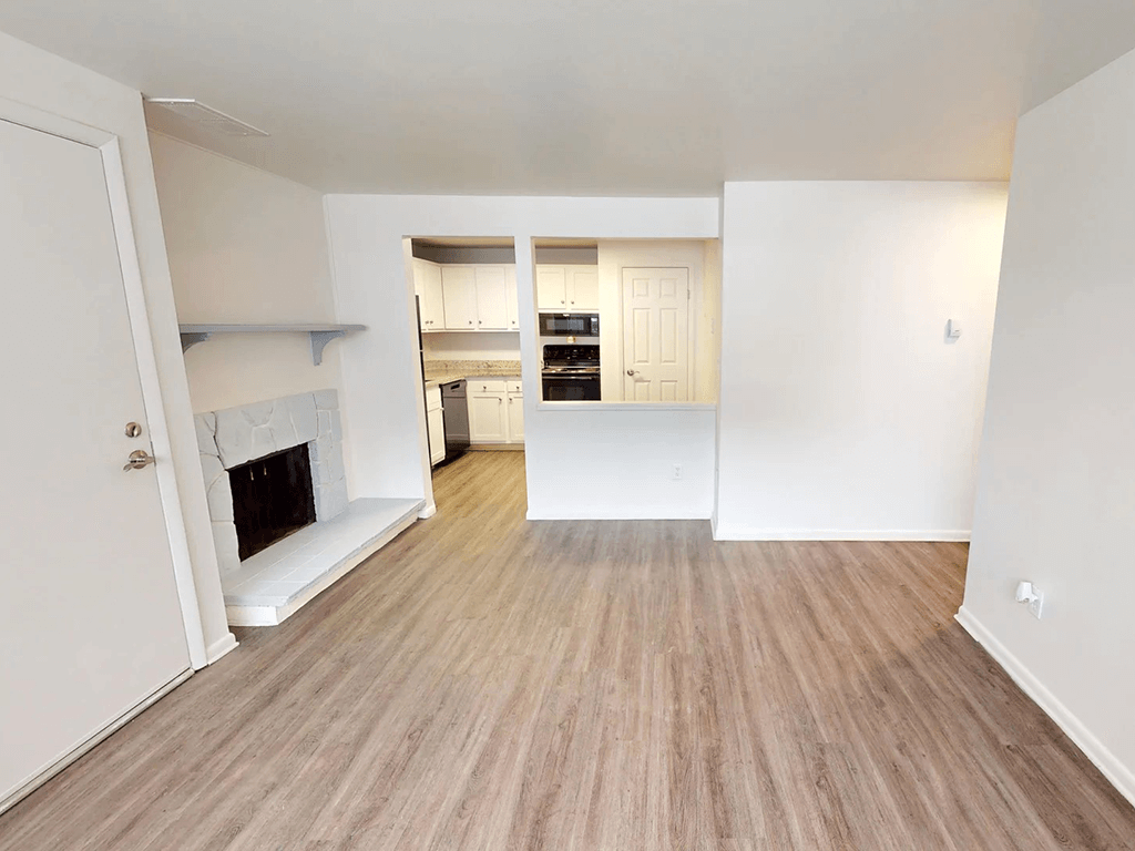 A room with a fireplace and a kitchen in the background.