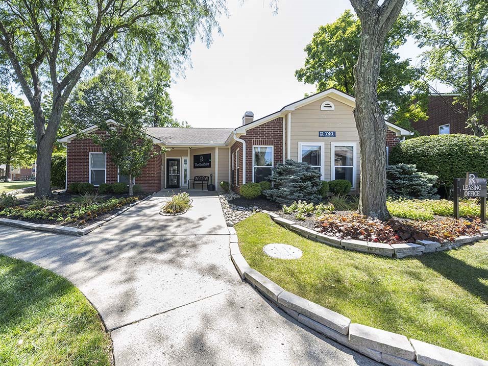 the front of a brick house with a driveway and trees
