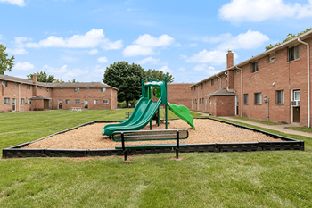 a playground with a green slide in a park in front of a brick building