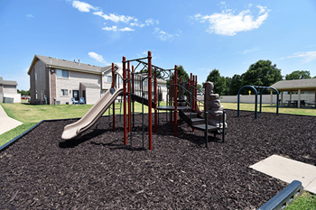A playground with a red slide and a green lawn.