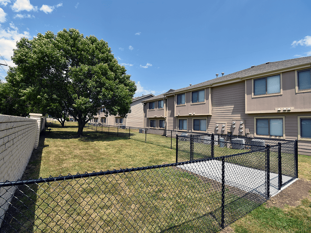 A black fence surrounds a grassy area in front of apartment buildings.