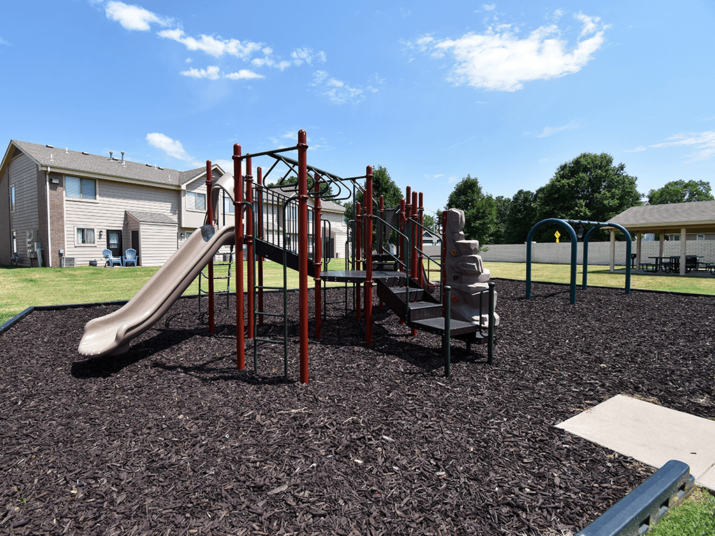 A playground with a red slide and a brown play structure.