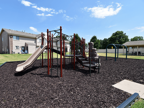 A playground with a red slide and a brown play structure.