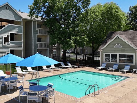 A pool surrounded by chairs and umbrellas in front of apartment buildings.