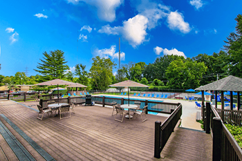 A wooden deck with tables and chairs overlooking a pool.