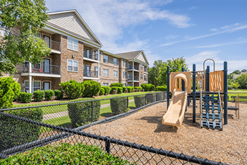 A playground with a slide and a climbing frame is in front of a building.