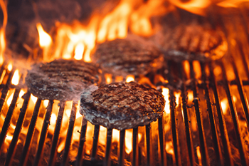 Two hamburgers cooking on a grill with flames in the background.