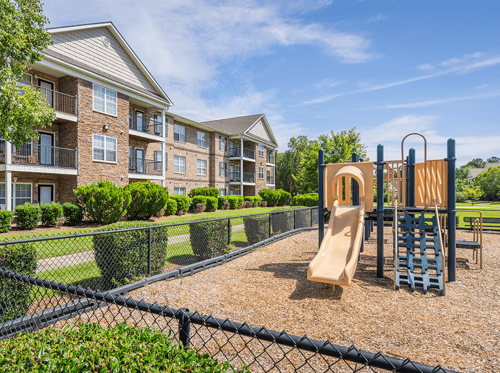 A playground with a slide and a climbing frame is in front of a building.