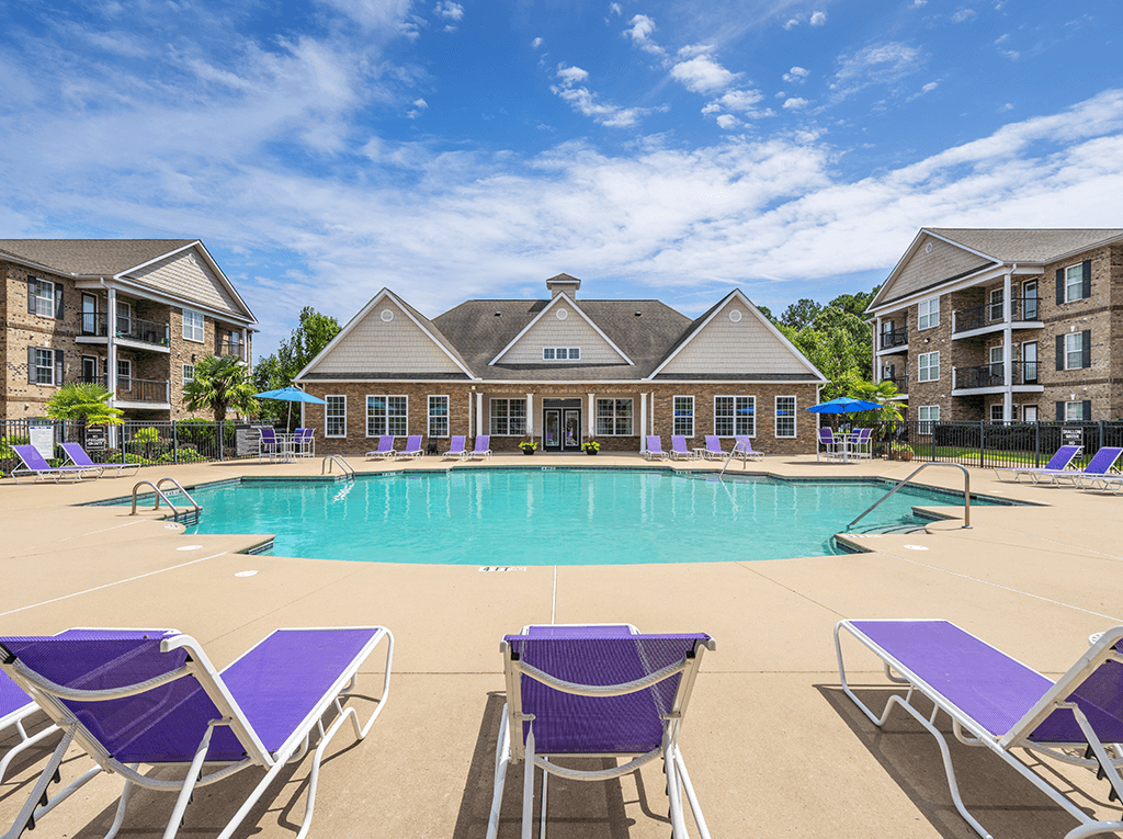 A large swimming pool surrounded by purple lounge chairs in front of apartment buildings.