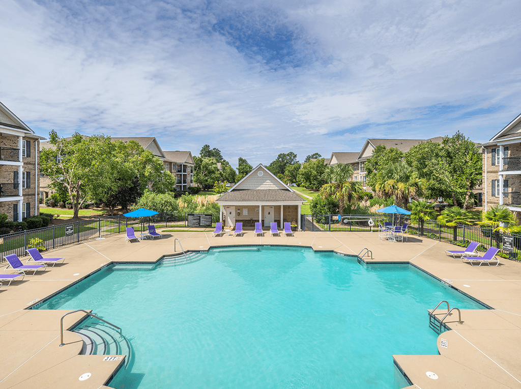 A large swimming pool surrounded by purple lounge chairs and a gazebo.