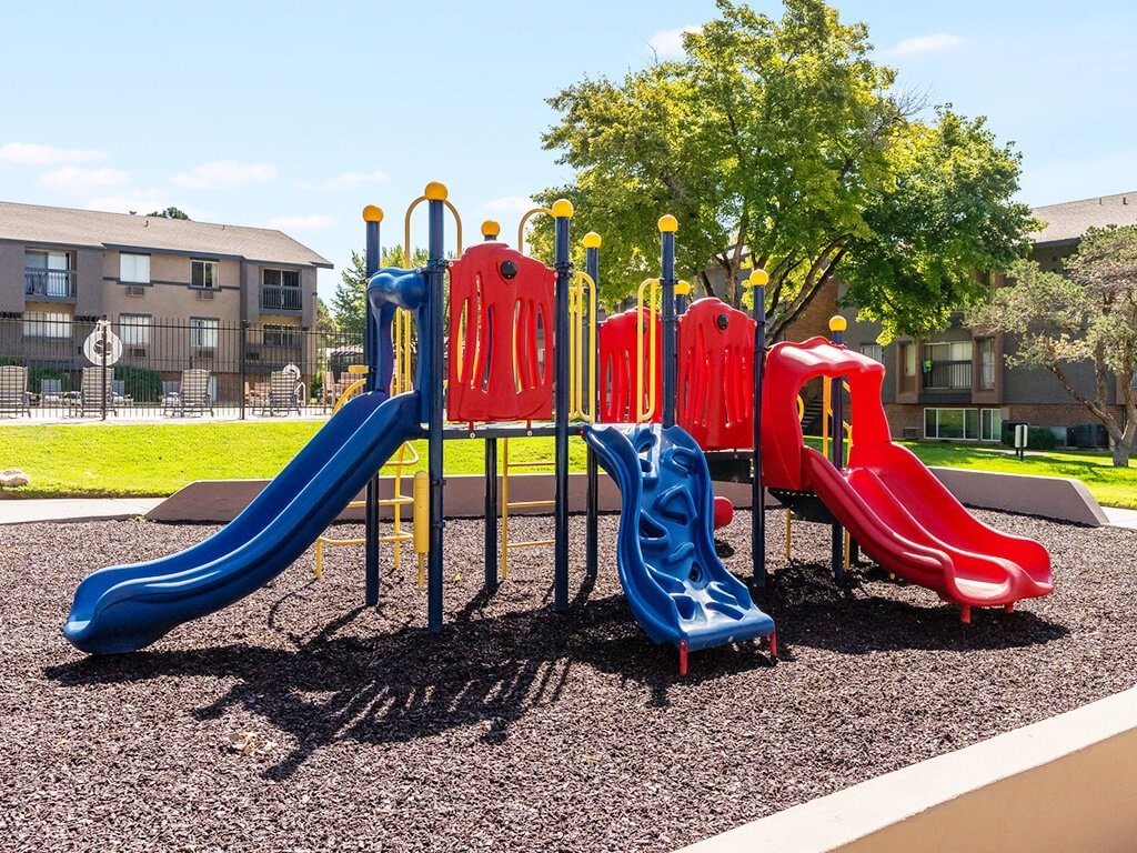 A playground with a blue and red slide and a yellow and red climbing structure.