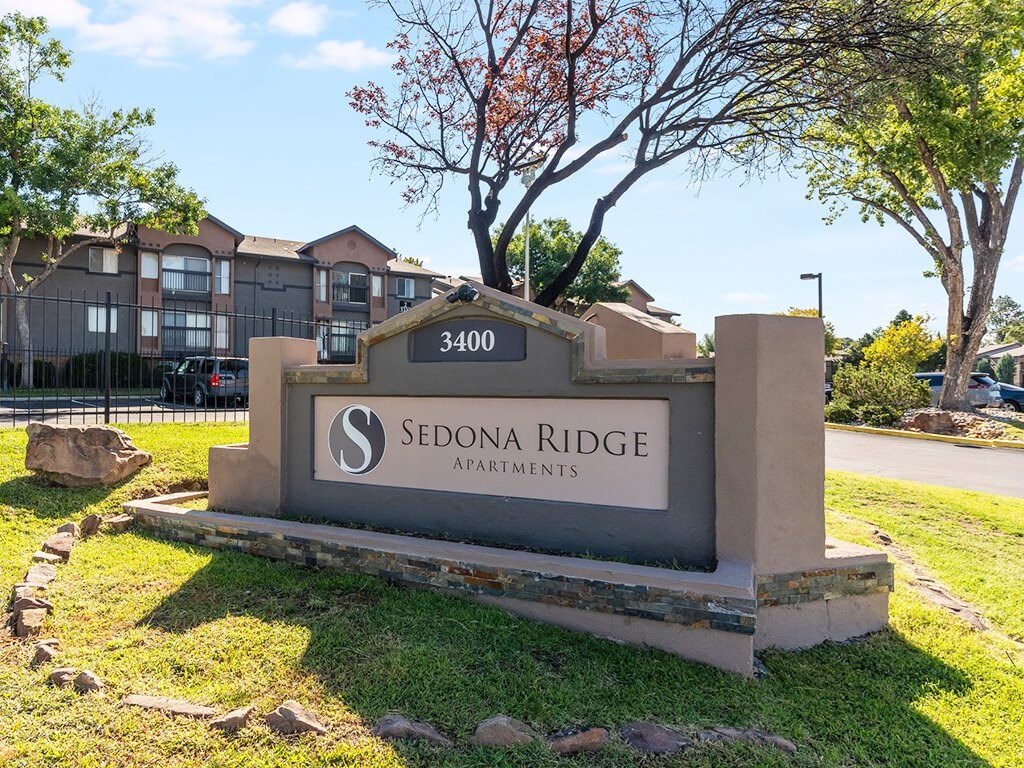 A sign for Sedona Ridge Apartments is in front of a tree and a building.