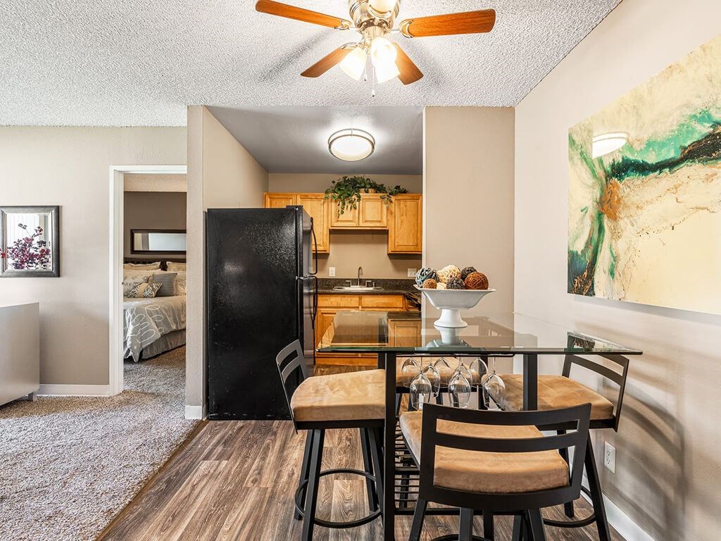 A kitchen with a black fridge and wooden chairs.