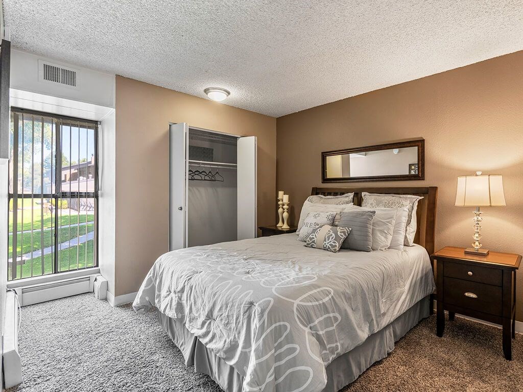 A bedroom with a large bed, a nightstand, and a window with a view of a lawn.