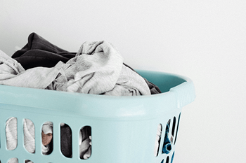 A light blue laundry basket filled with a grey and black pile of clothes.