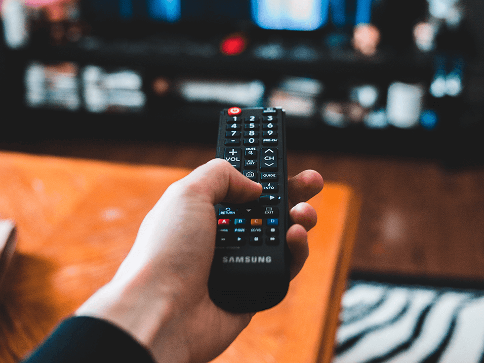 a hand holding a remote control with a television in the background