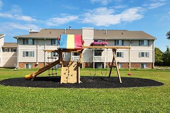 A playground with a slide and swings in front of a building.