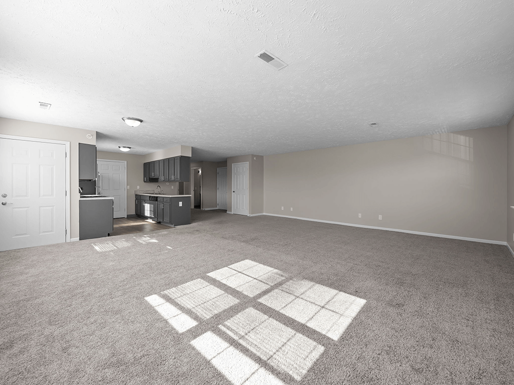 an empty living room with a kitchen in the background