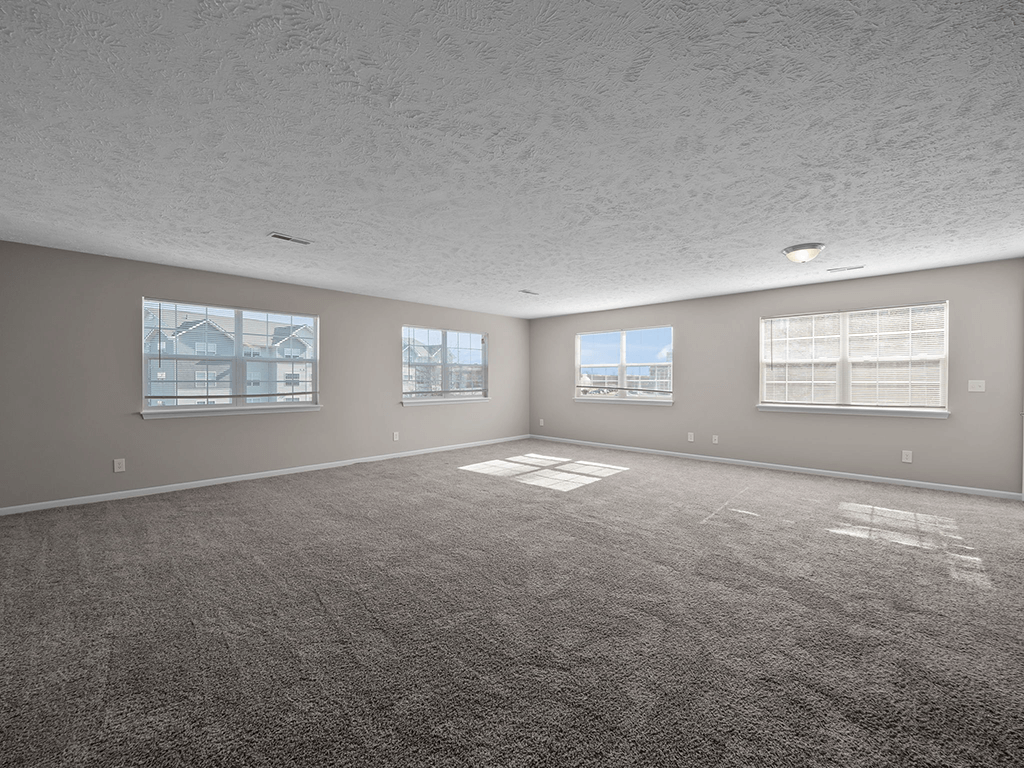 an empty living room with a carpeted floor and three windows