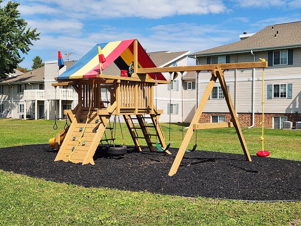 A wooden swing set with a red ball on the ground.