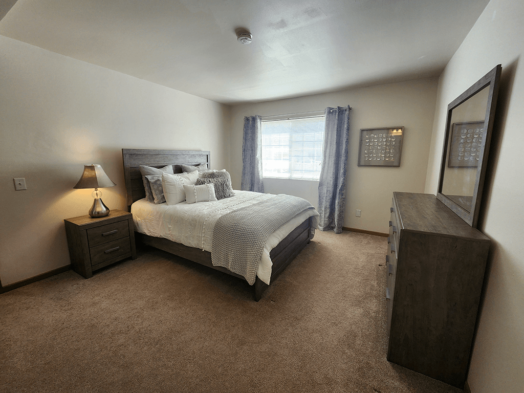 A bedroom with a large bed and a nightstand with a lamp.