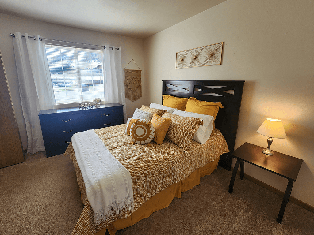 A bedroom with a bed, nightstand, and window.