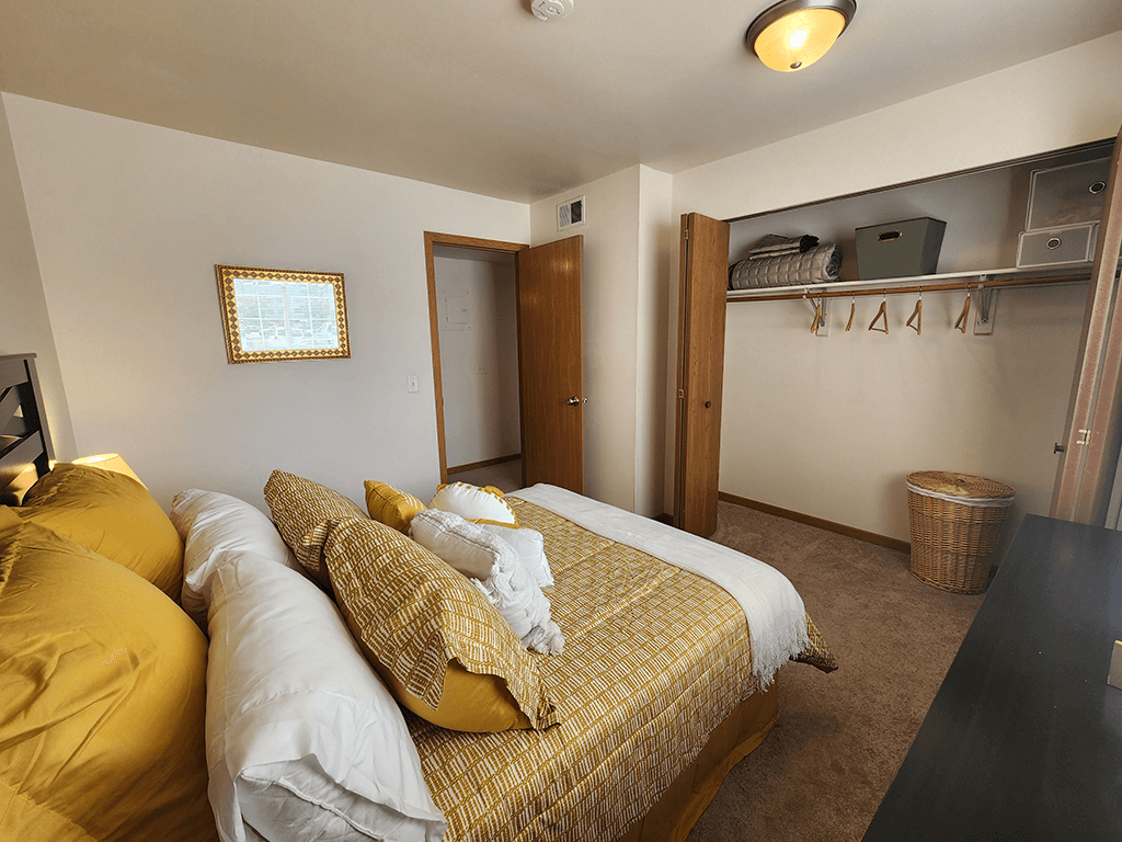 A bedroom with a bed covered in yellow and white bedding.