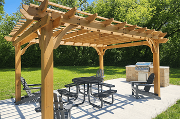 A wooden pavilion with a table and chairs and grill