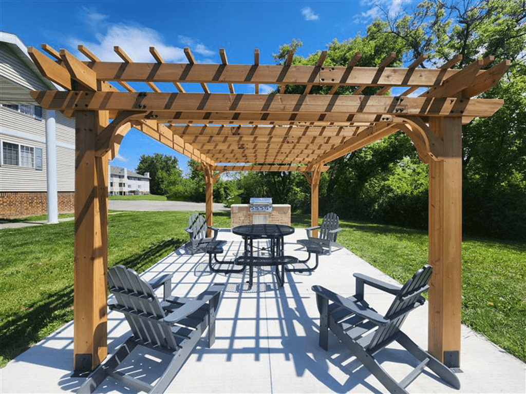 A wooden pavilion with a table and chairs and grill