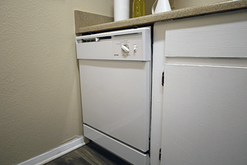 A white dishwasher is in a kitchen next to a white wall.
