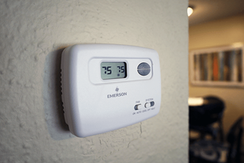 A white thermostat on a wall with the number 75 displayed.