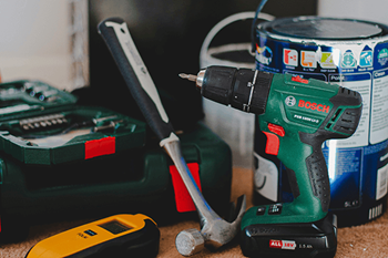 A green Bosch drill is on a table with a hammer and a yellow and black device.