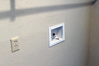 A white electrical outlet with a white switch box on a white wall.