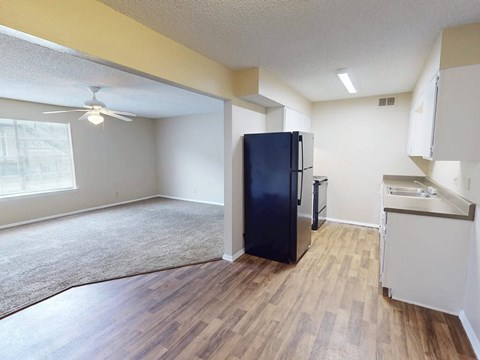 A black fridge in a kitchen with wooden floors and white walls.