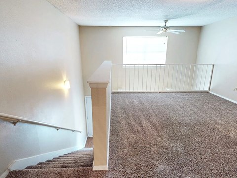 A room with a carpeted floor and a staircase leading to another room.